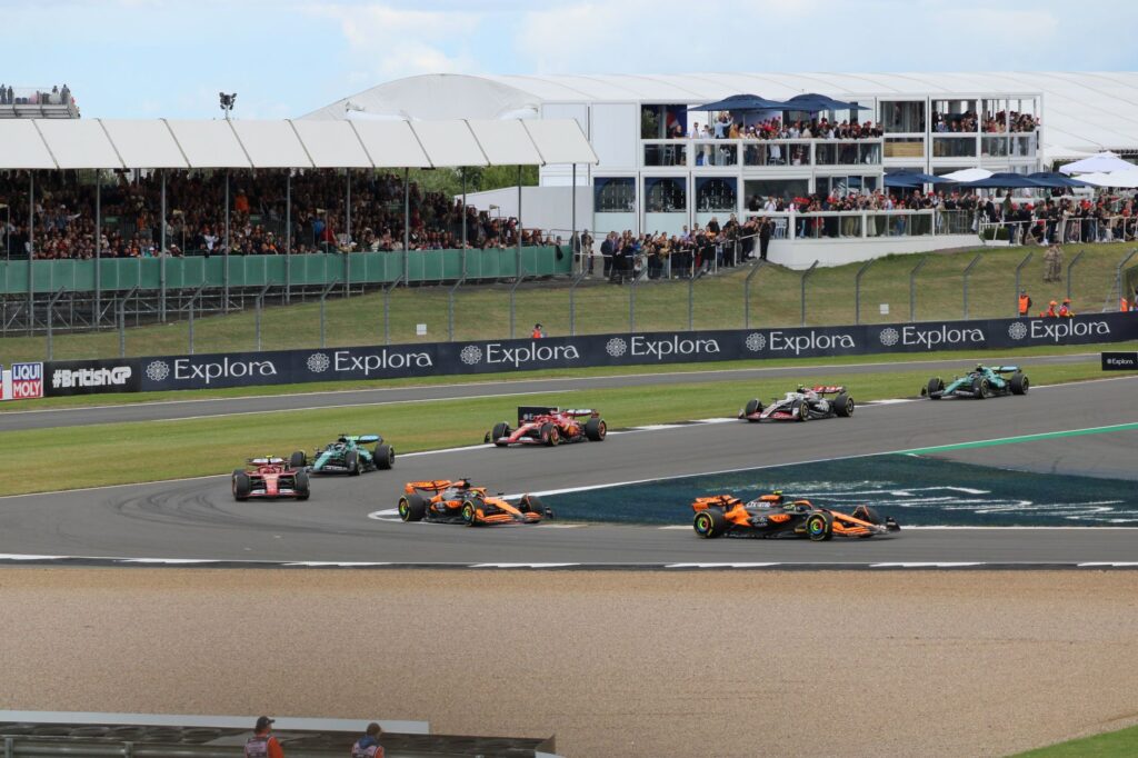 Thrilling car race at Silverstone Circuit with packed grandstands and vibrant crowd.