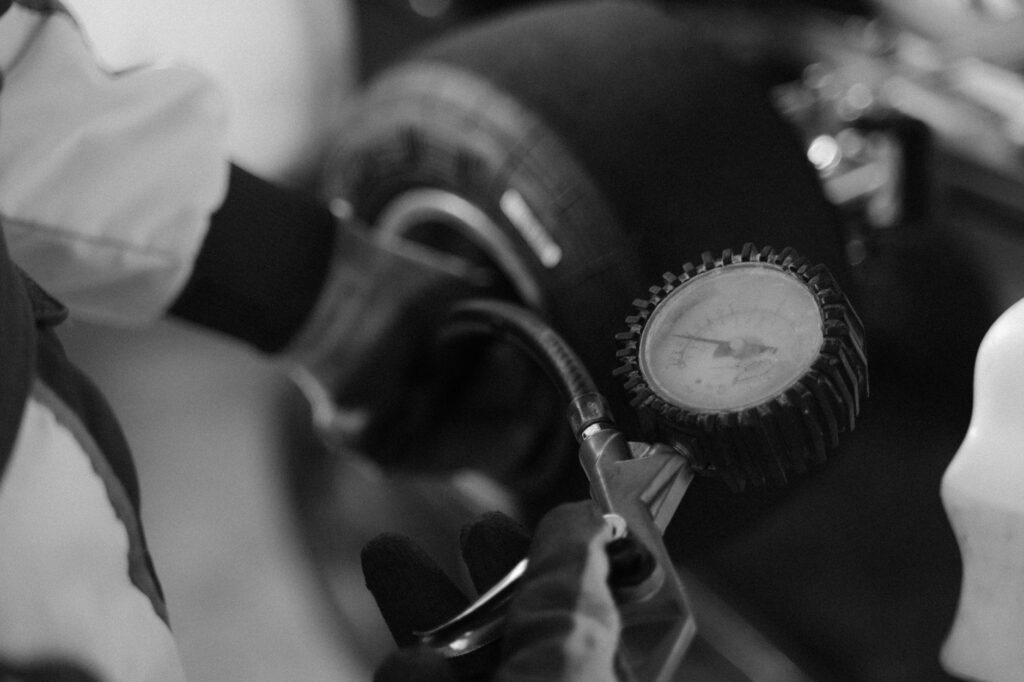 Black and white image of a mechanic using a gauge to check tire pressure on a kart wheel.