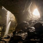 Dramatic cave view with backlit entrance and cascading waterfalls creating a mystical atmosphere.