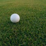 A close-up image of a golf ball resting on vibrant green grass, perfect for sports and recreation themes.
