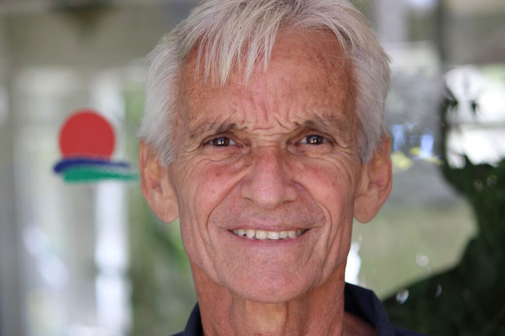 Close-up portrait of a smiling senior man with bright eyes and white hair.