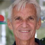 Close-up portrait of a smiling senior man with bright eyes and white hair.
