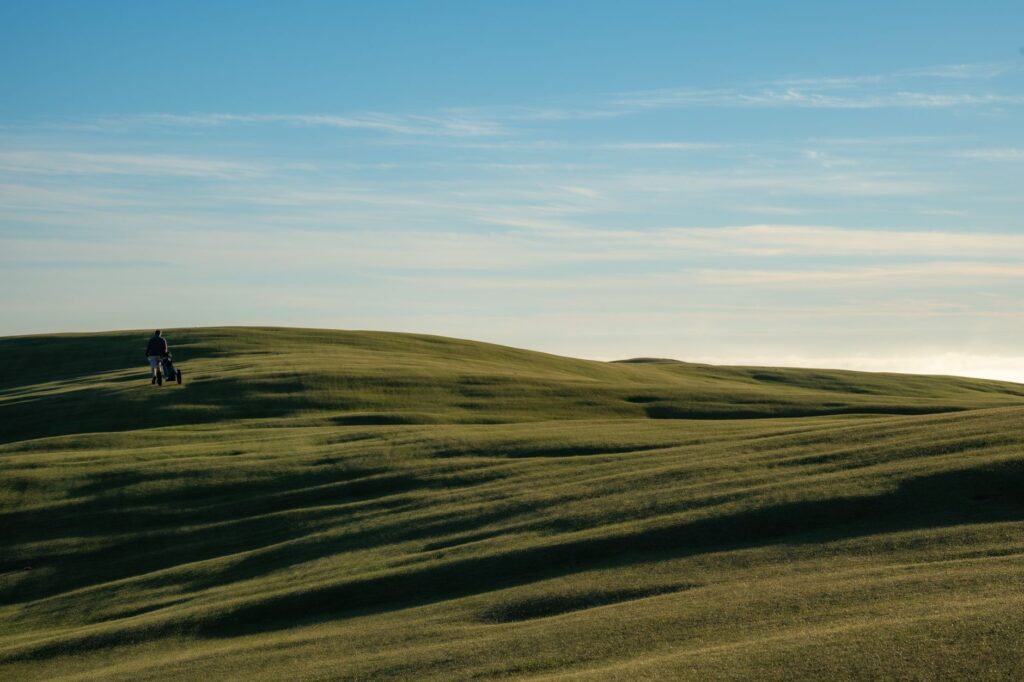 A solitary person walking on rolling green hills under a blue sky.