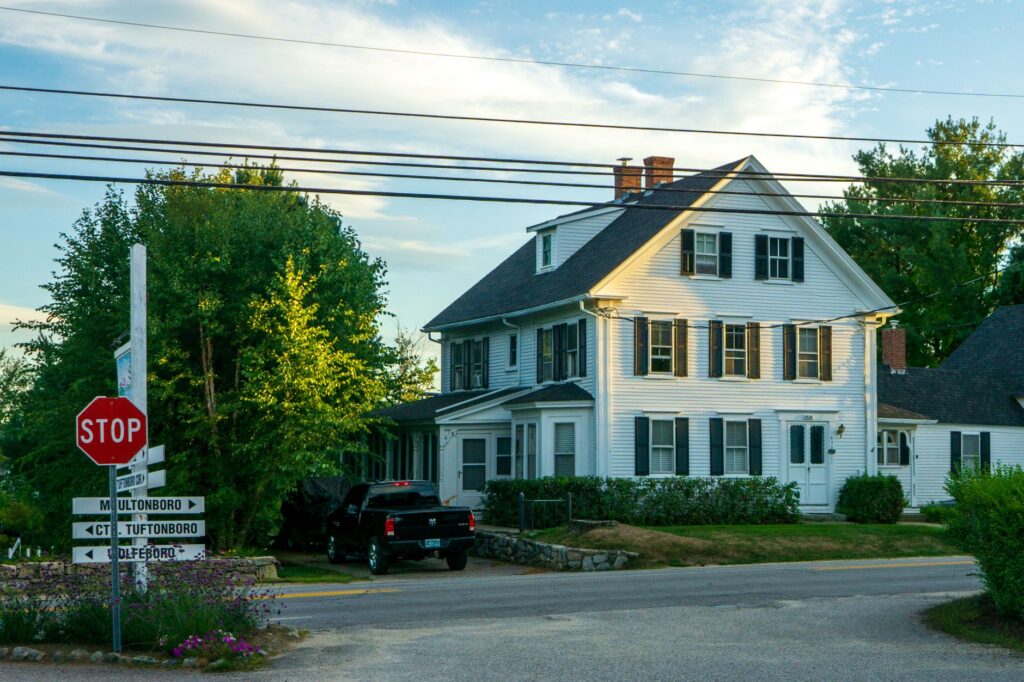 Quaint colonial house at suburban street with cars and road signs under clear sky.