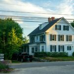 Quaint colonial house at suburban street with cars and road signs under clear sky.