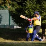 Action shot of a cricketer batting during an outdoor match on a sunny day.