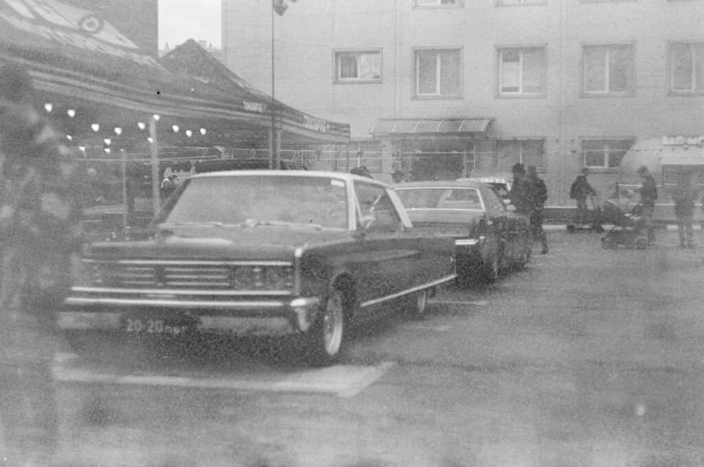 Black and white photo of classic cars parked in a city market setting, evoking a vintage feel.