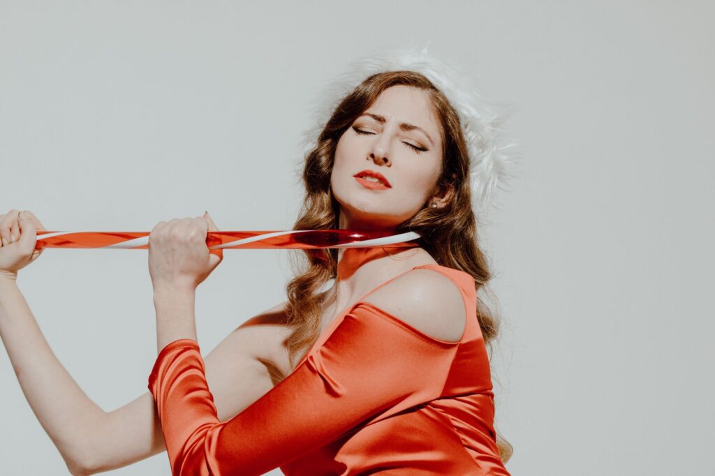 Elegant woman in a Santa hat posing with festive ribbon in a winter-themed studio portrait.