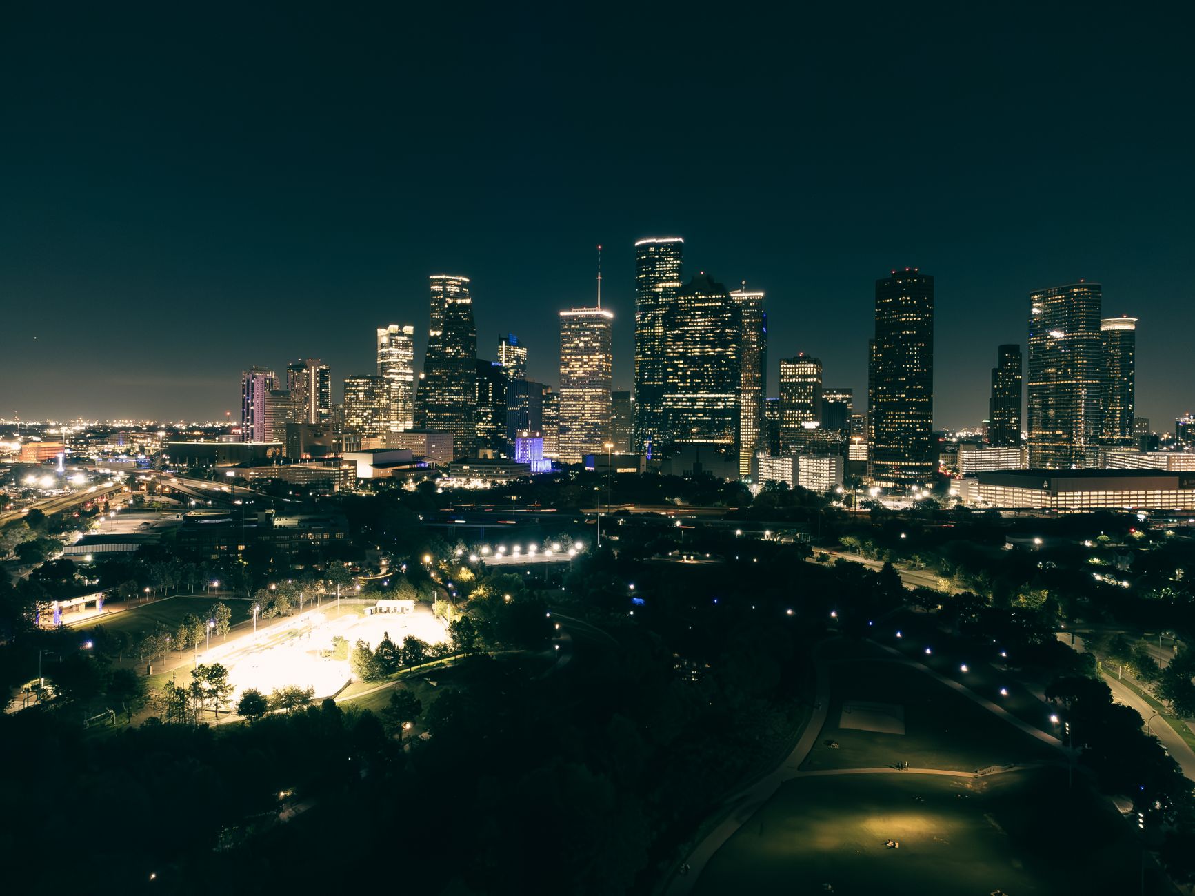 A stunning aerial view of Houston's illuminated skyline at night, showcasing skyscrapers and urban parks.