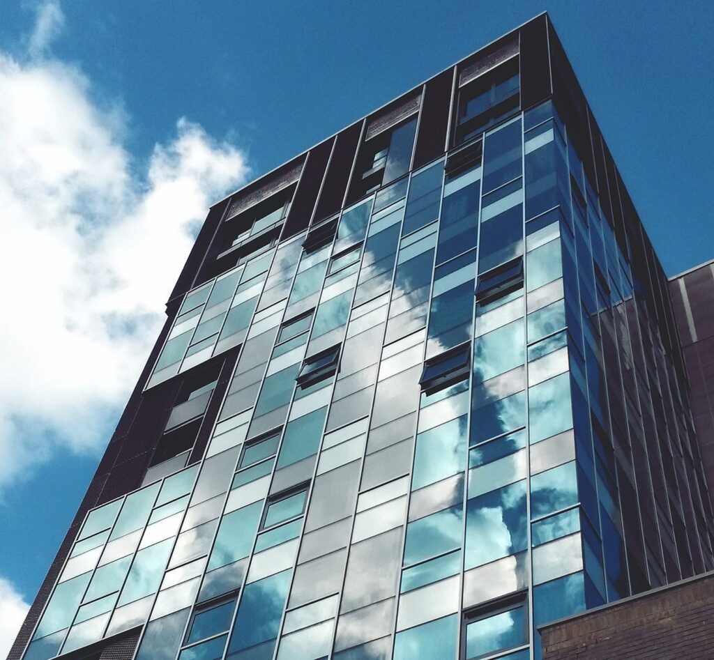 Low-angle view of a glass facade building with sky reflections in Norwich.