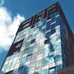 Low-angle view of a glass facade building with sky reflections in Norwich.