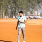 Young man in sportswear walking alone on an outdoor dirt field during daytime.