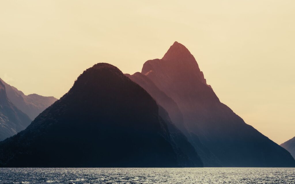 Dramatic sunset over Milford Sound, New Zealand, highlighting the majestic mountains and serene sea.