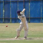 Cricket player in action, batting on a grass field in Gahunje, India.