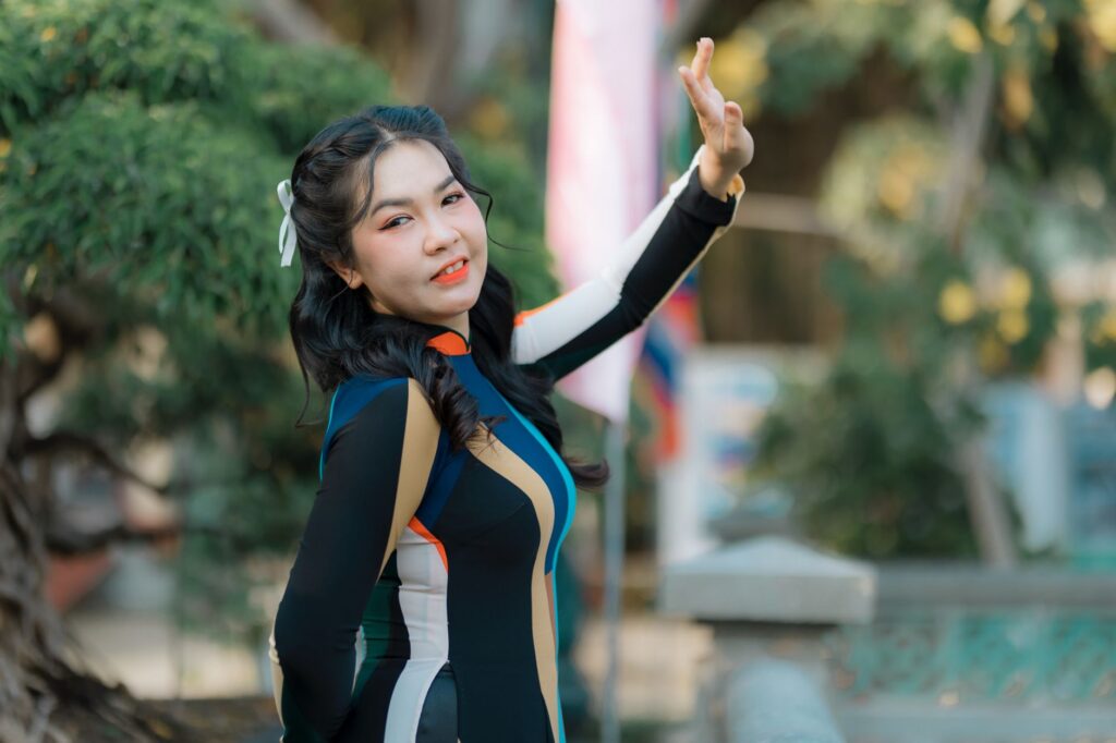 Smiling woman in colorful dress posing with hand raised in a sunny outdoor setting.