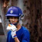 A young cricket player in Pune wearing a helmet and gloves, ready for the game.