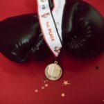 Black boxing gloves with a gold medal on a red background, symbolizing victory and success.