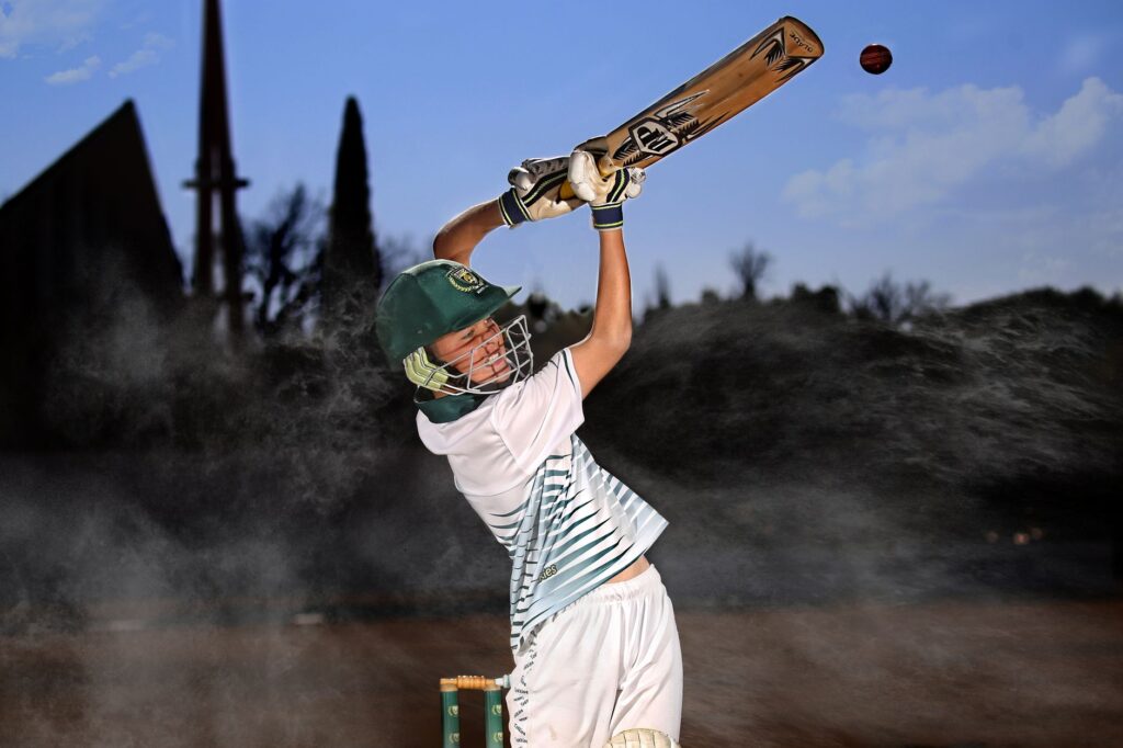 An energetic batsman in motion hitting a cricket ball in an outdoor field.
