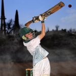 An energetic batsman in motion hitting a cricket ball in an outdoor field.