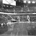Through glass black and white football team standing together and congratulating each other with match win game in crowded stadium