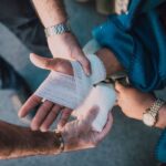 Close-up of two people bandaging an injured hand outdoors, focusing on first aid care.