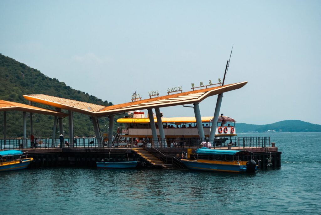 Scenic view of a modern pier in Hong Kong with boats, calm water, and a hillside landscape on a sunny day.