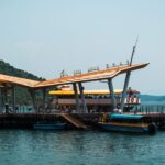 Scenic view of a modern pier in Hong Kong with boats, calm water, and a hillside landscape on a sunny day.