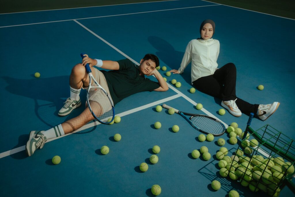Young adults sit with tennis rackets and balls on an outdoor court, enjoying a relaxed moment.