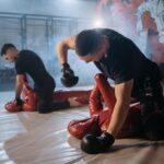Two fighters practice ground and pound techniques on dummies in a gym setting.
