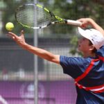 Teenage tennis player in action serving on a sunny outdoor court.