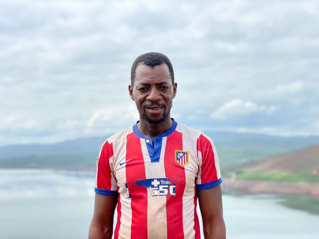 Portrait of a smiling African man in a striped jersey with a scenic outdoor landscape in Guinea.