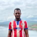 Portrait of a smiling African man in a striped jersey with a scenic outdoor landscape in Guinea.