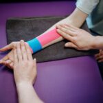 A therapist carefully applying colorful kinesiology tape on a patient's forearm for supportive therapy.