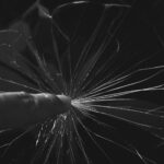 Black and white close-up of a finger touching a cracked glass screen, creating a dramatic effect.