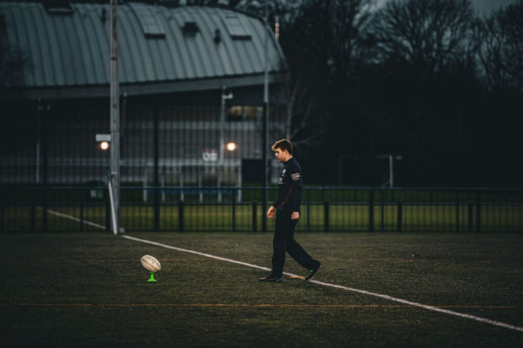 Rugby player sets up for a kick on an empty field in England.