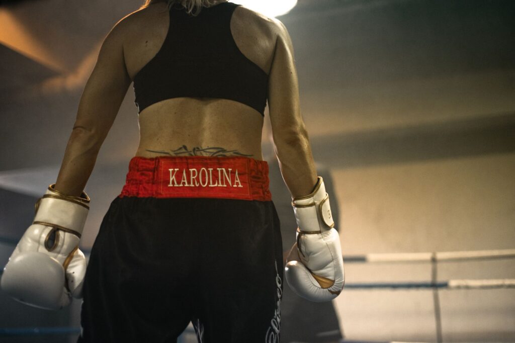 A focused female boxer preparing in the ring, wearing gloves and gym clothes, demonstrating determination.