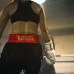 A focused female boxer preparing in the ring, wearing gloves and gym clothes, demonstrating determination.