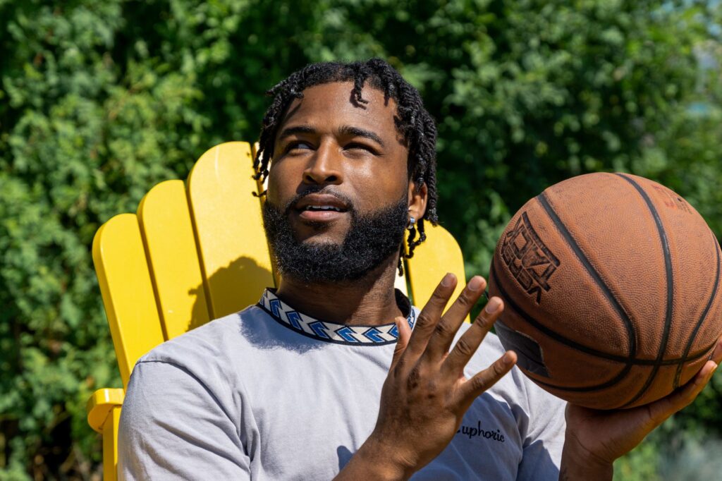 A young man sits outdoors holding a basketball, enjoying a sunny day.