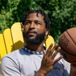 A young man sits outdoors holding a basketball, enjoying a sunny day.