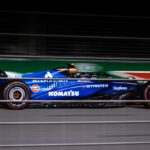 Blue Formula car speeding on track during night race.