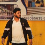 A cricket player on a turf field wearing a jacket with a focused look.