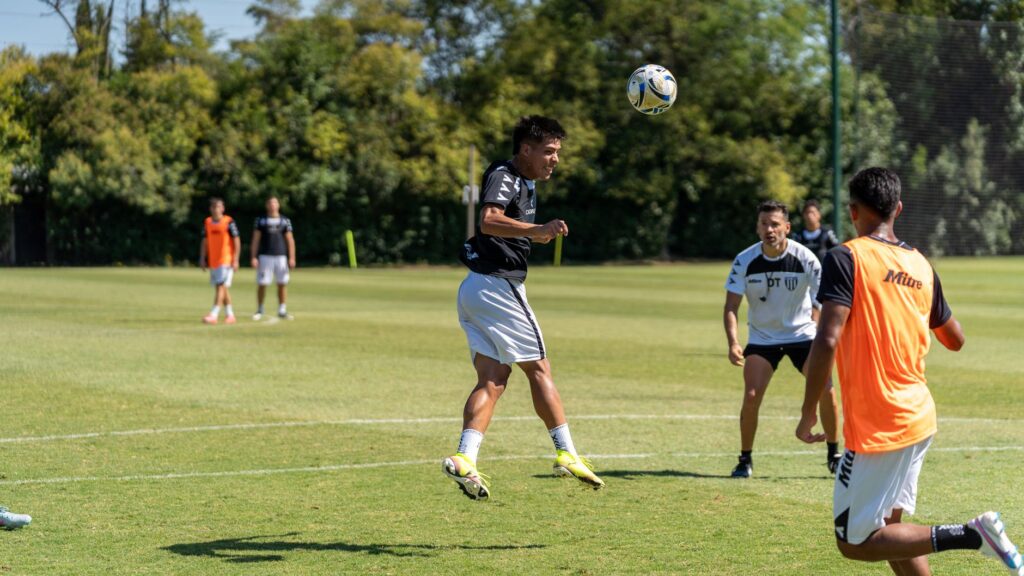 Athletes practicing heading skills during an outdoor soccer training session on a sunny day.