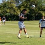 Athletes practicing heading skills during an outdoor soccer training session on a sunny day.