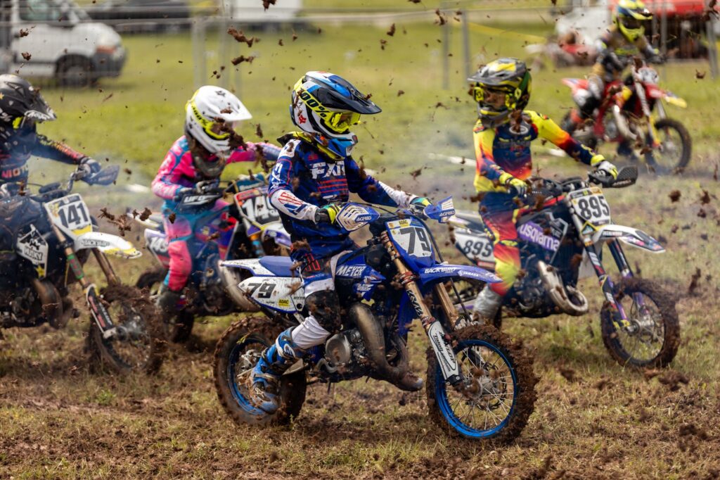 Exciting youth motocross race on a muddy track showcasing young riders in action-packed competition.