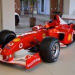 A striking red Formula 1 Ferrari race car displayed in a modern showroom setting.