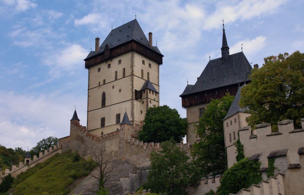 View of the medieval Karlštejn Castle surrounded by greenery under a cloudy sky.