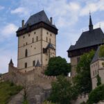 View of the medieval Karlštejn Castle surrounded by greenery under a cloudy sky.