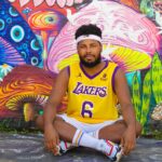 Man sitting against a vibrant mural wearing a Lakers jersey in São Paulo, Brazil.