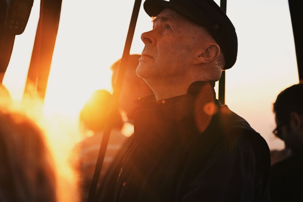 Profile of an elderly man in a hat gazing at a sunset, with dramatic lighting.