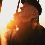 Profile of an elderly man in a hat gazing at a sunset, with dramatic lighting.